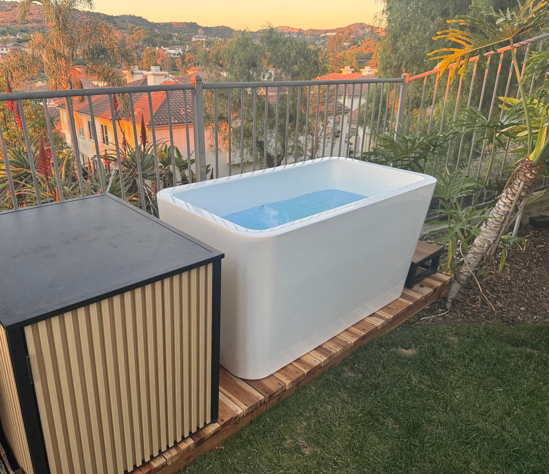 White cold plunge tub with chiller cabinet on a wooden platform in a backyard at dusk
