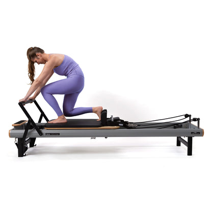 Peak Pilates casa Reformer with Long/Short Box in use as a woman performs a kneeling leg exercise at home